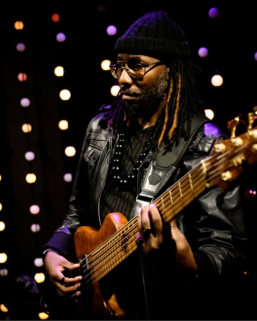Errick Lewis playing his white five-string bass under red stage lighting.